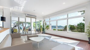 Un amplio y moderno salón con grandes ventanales que ofrecen vistas al mar y a la ciudad.
