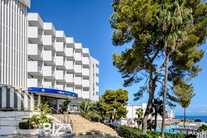 Un hotel moderno con fachada geométrica, zona de piscina y vista despejada al mar.