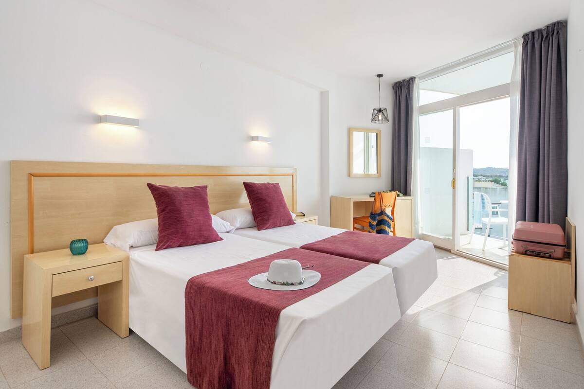 A hotel room with a large bed, two bedside tables, a suitcase, and a view of the city.