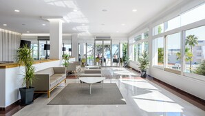 Un vestíbulo amplio con mostrador de recepción, zona de estar y ventanas grandes que ofrecen vistas al exterior.