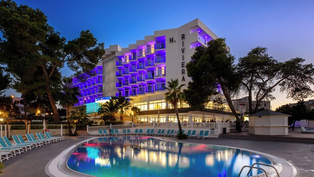 Un hotel con piscina, sillas de descanso y una fachada bien iluminada.