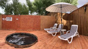 Relax in a serene outdoor space with a hot tub and lounge chairs, shaded by a large umbrella.