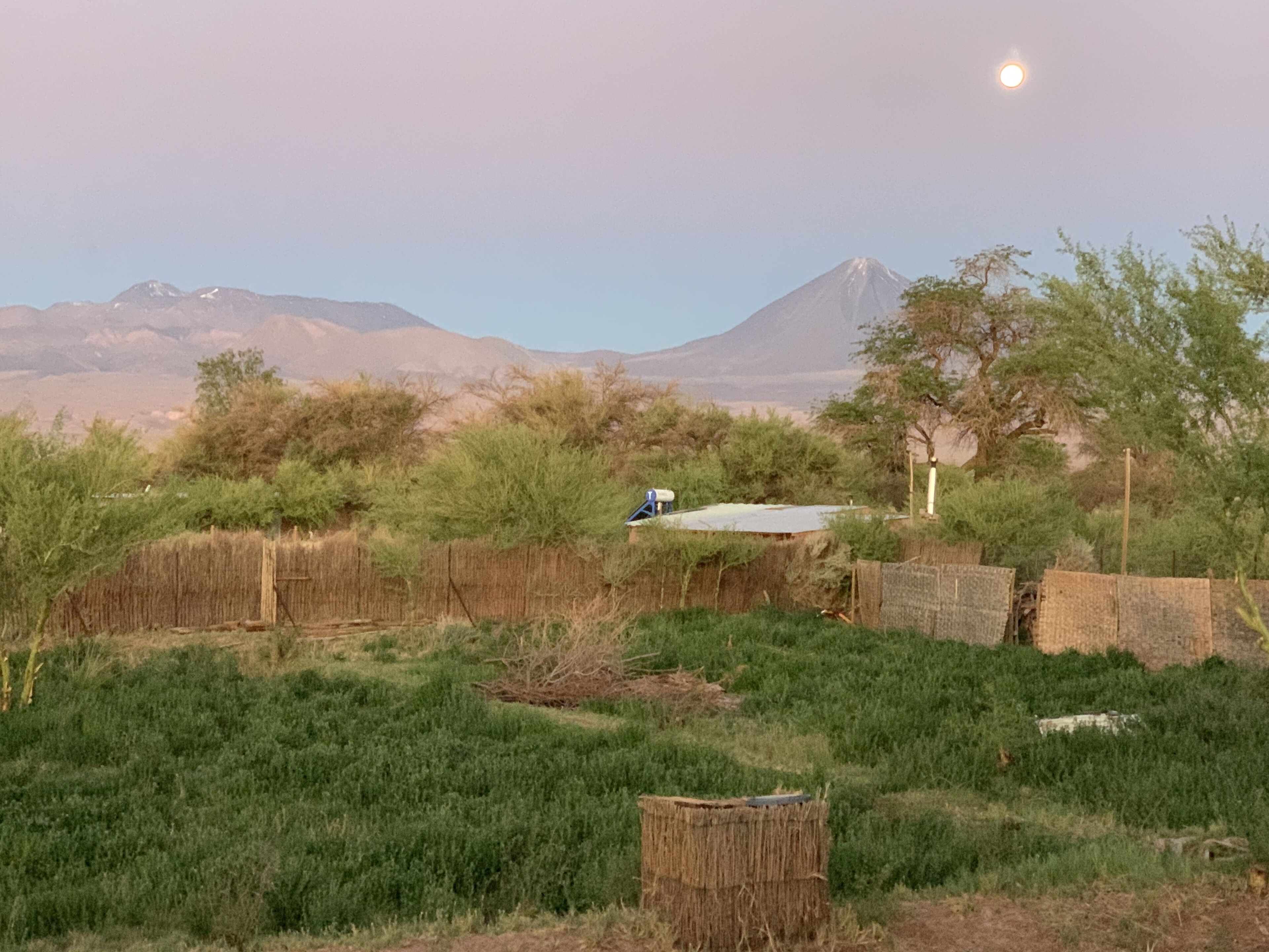 Paisagem rural com uma montanha ao fundo, um trator azul e um fardo de palha em primeiro plano.