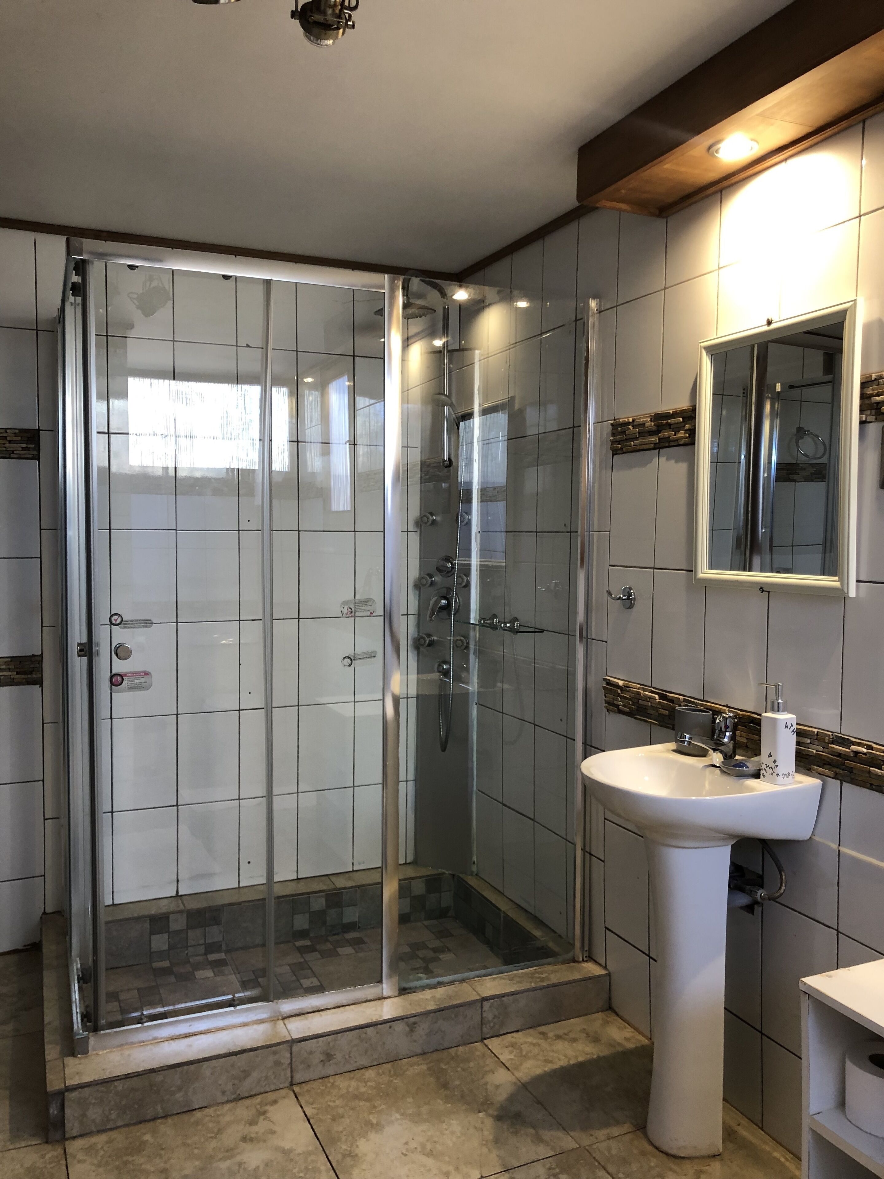 Un baño moderno con ducha de vidrio, un lavamanos blanco y un espejo sobre él.