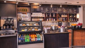 Una cafetería con un mostrador refrigerado, una máquina de café y una pizarra de menú.