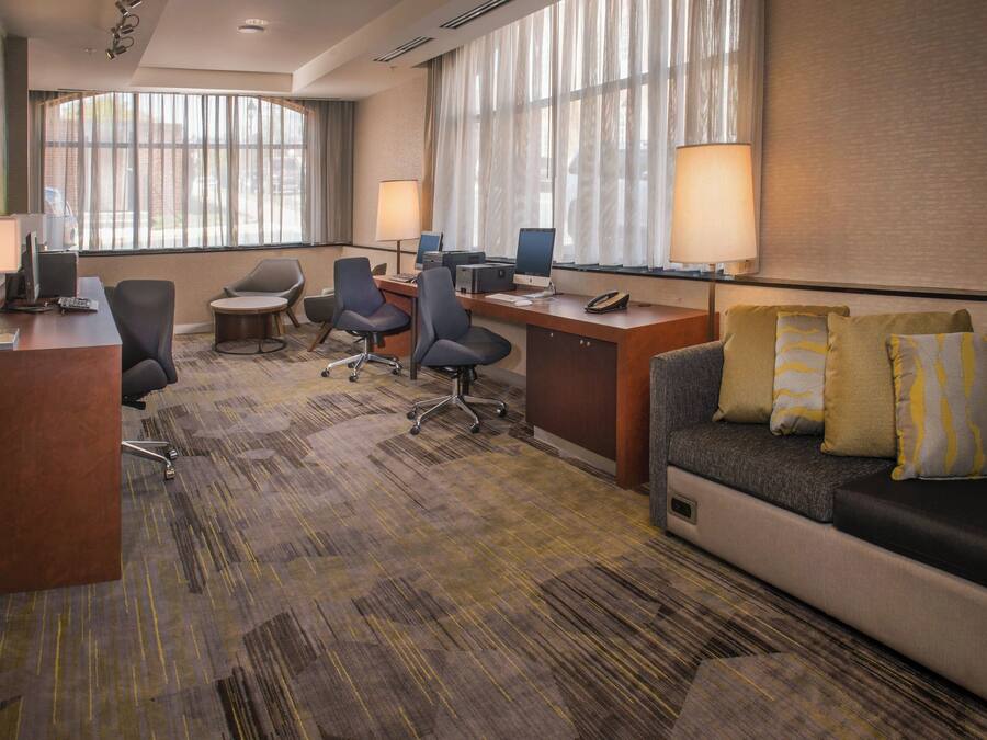 A hotel room with a desk, two chairs, a sofa, and a large window with curtains.