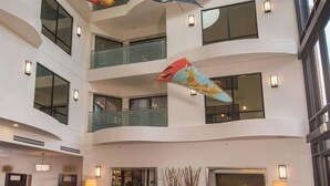 Un hall de hotel de varios niveles con zonas de estar, ventanas amplias y elementos decorativos colgantes.