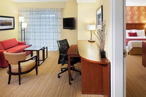 Una habitación de hotel con un sofá rojo, un escritorio de madera, una silla de oficina negra, un televisor y una cama con ropa de cama blanca.