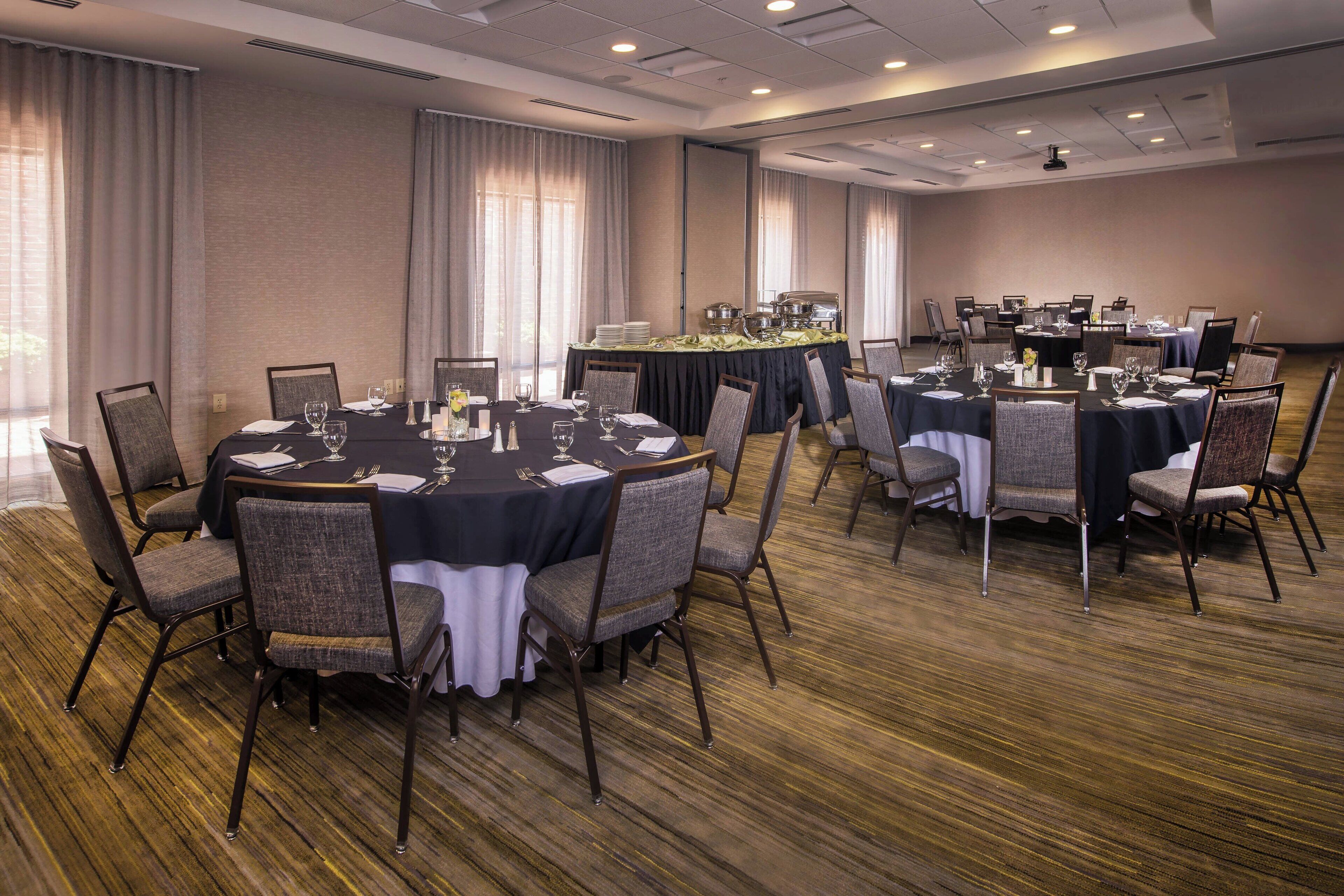 Un salón de conferencias con mesas redondas, sillas y una zona de buffet.