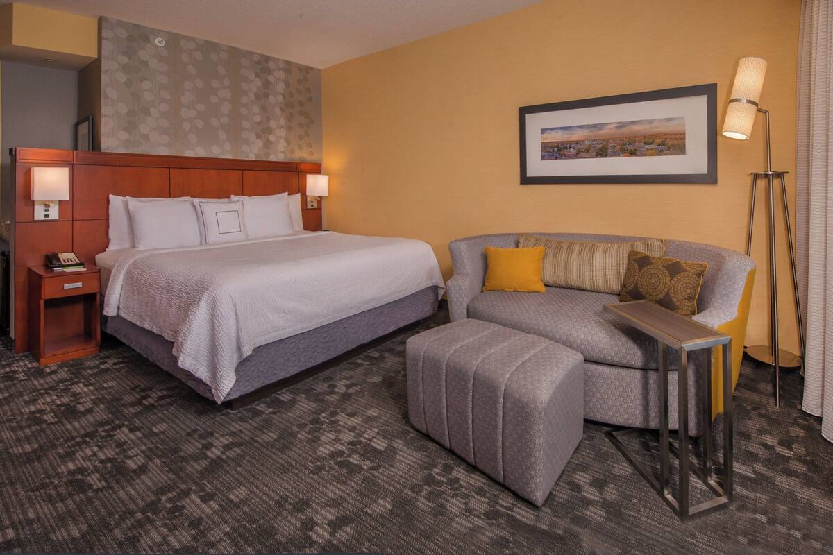 A hotel room with a large bed, a sofa, a small table, and a floor lamp.