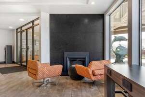 Un vestíbulo moderno con dos sillones de estampado naranja, una chimenea oscura y un ventanal con vistas a una escultura.