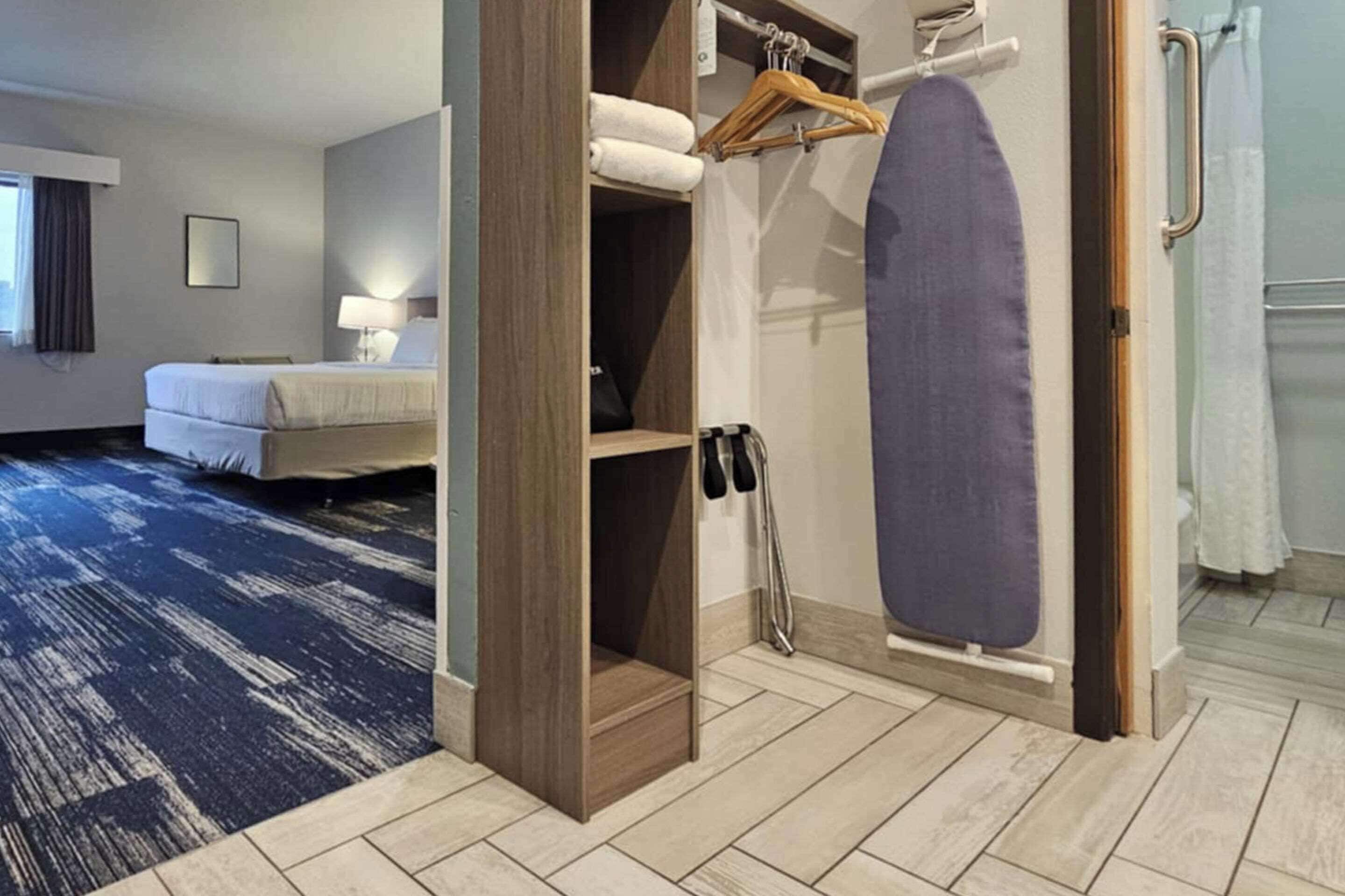 A hotel room with a bed, a wooden wardrobe, a hanging rack with clothes, and a shower area.