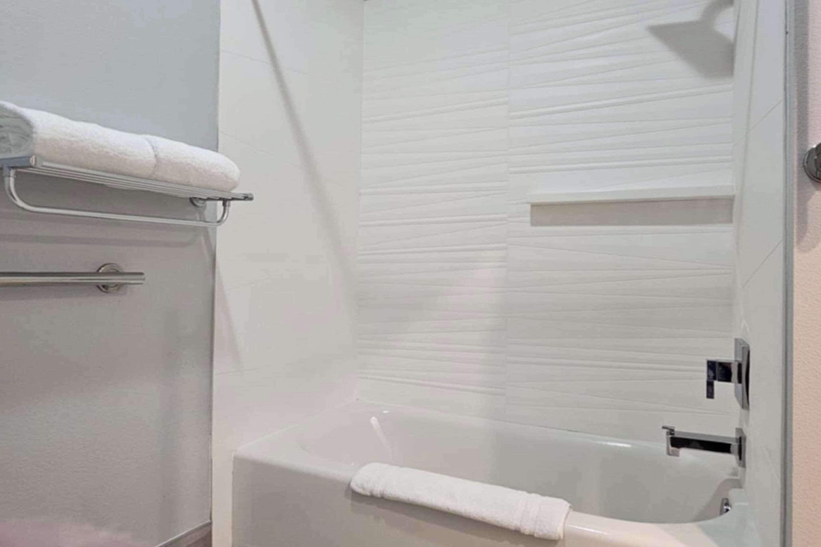 A modern bathroom with a glass-enclosed shower, a white bathtub, and a towel rack.