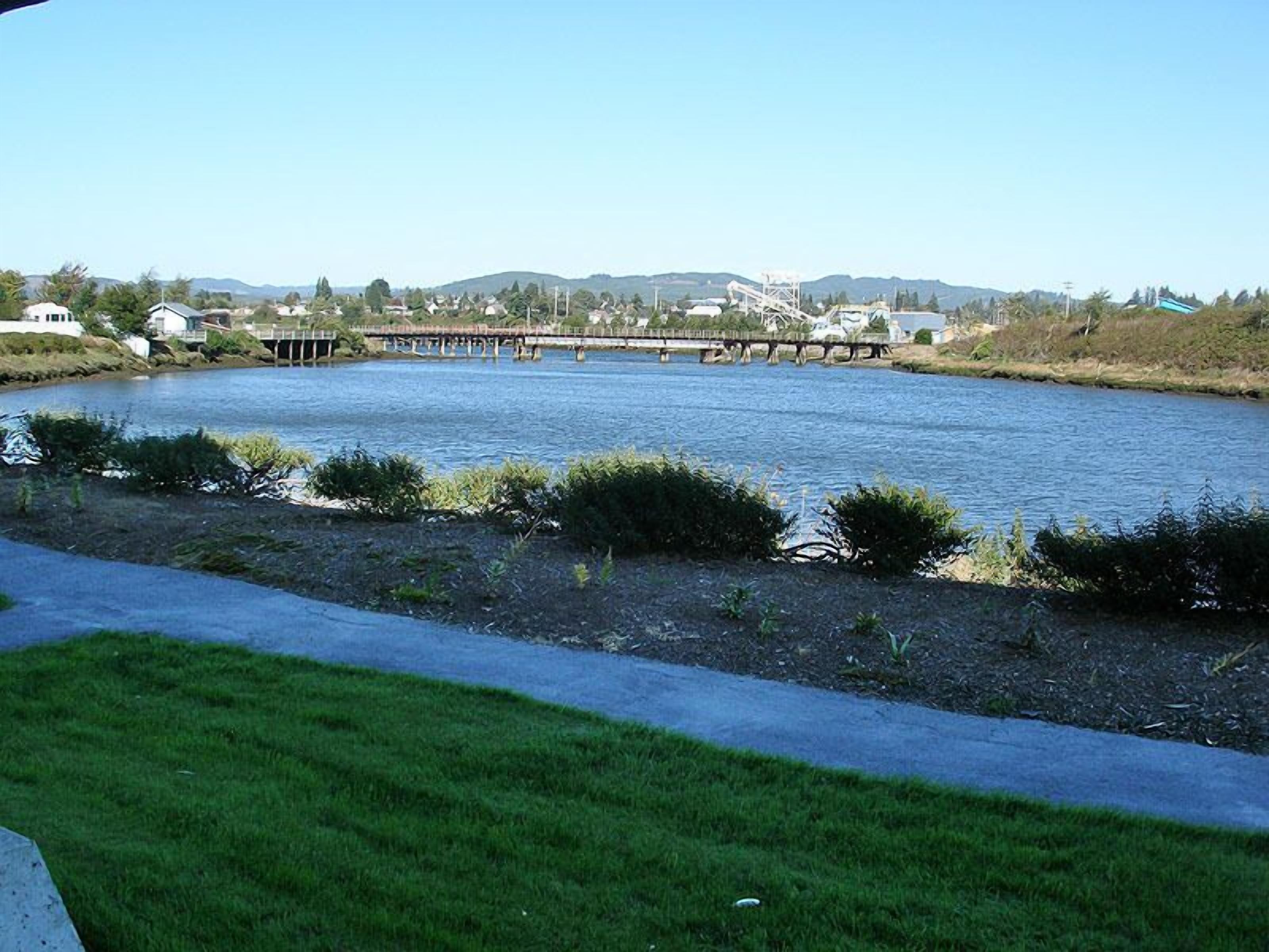 A river with a bridge, grassy banks, and buildings in the background.