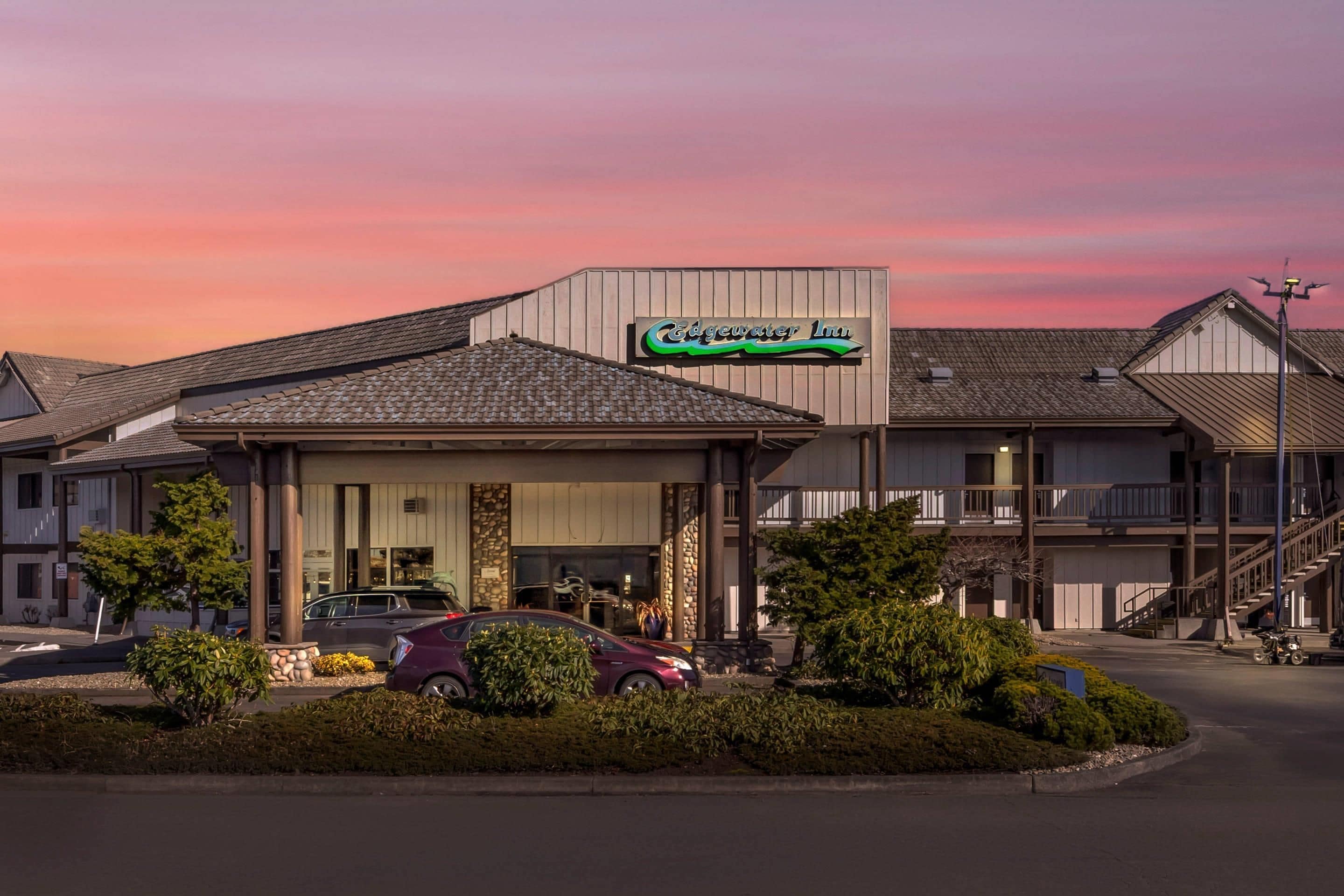 A hotel with a prominent sign, a covered entrance, and a parking area with cars.