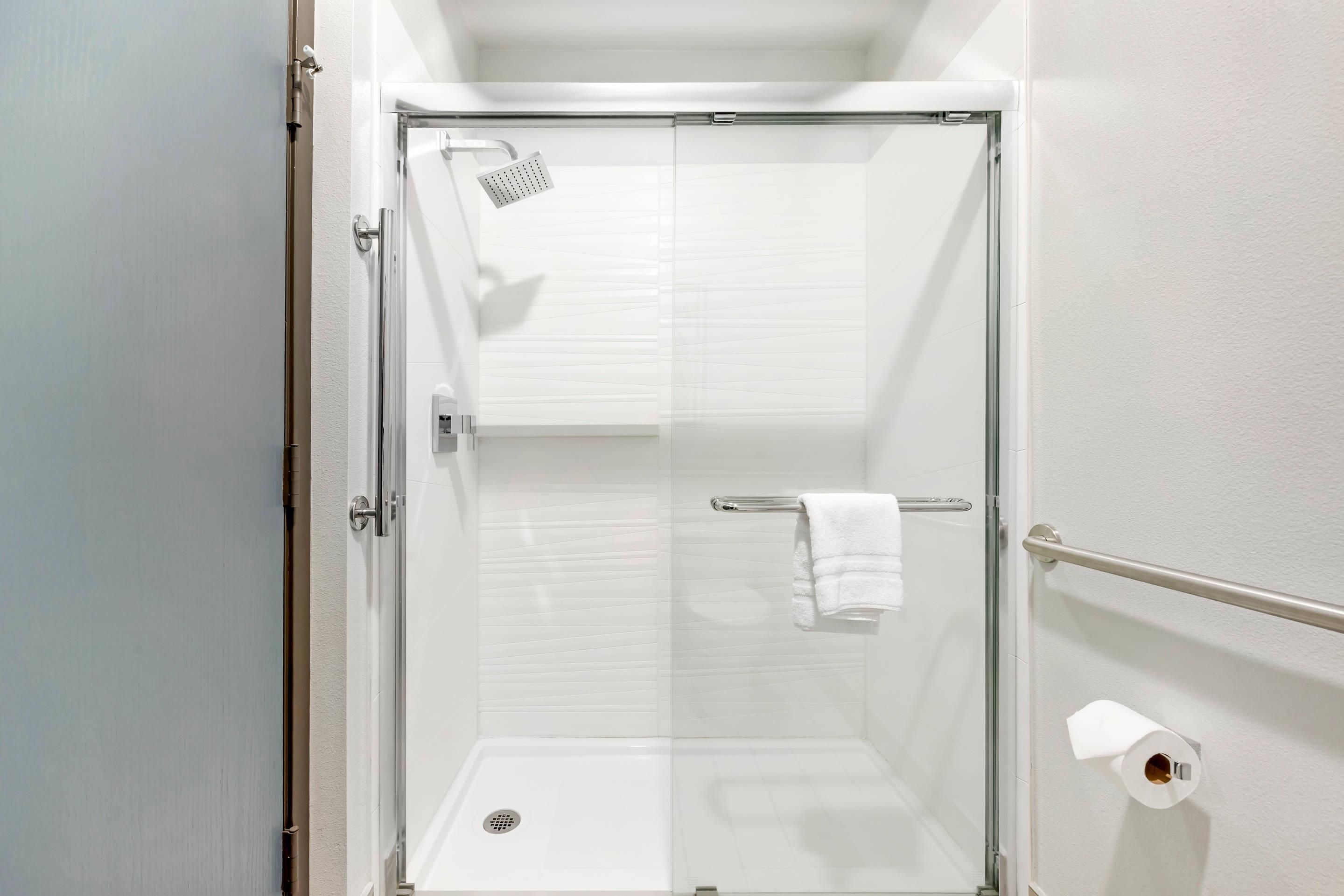 A glass-enclosed shower stall with a white towel rack and a toilet paper holder.