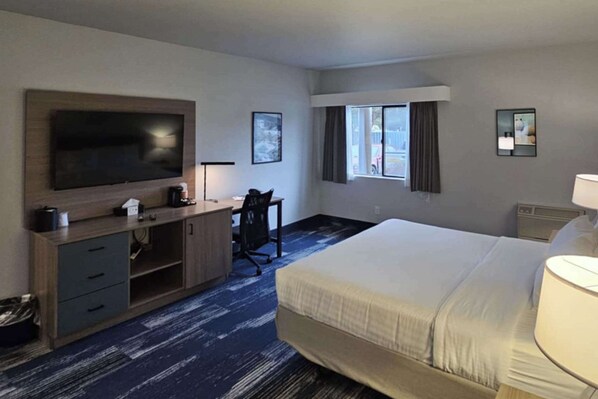 Une chambre d’hôtel avec un grand lit, un bureau avec une chaise, une télévision et une fenêtre avec des rideaux.