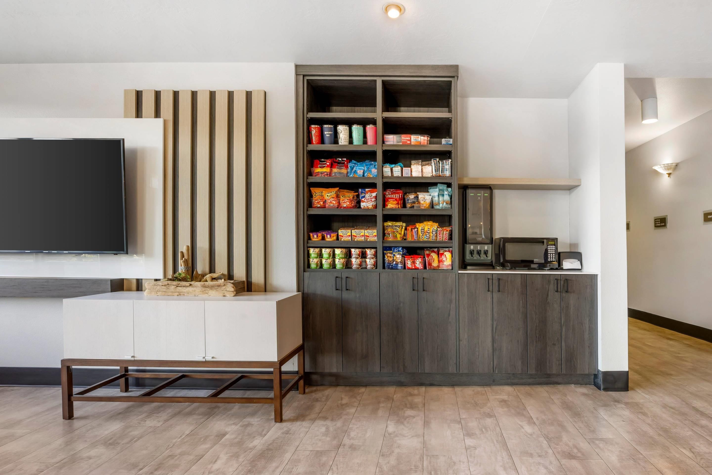 Una sala de estar moderna con un televisor de pantalla plana, un mueble de madera con aperitivos, un microondas y una cafetera.