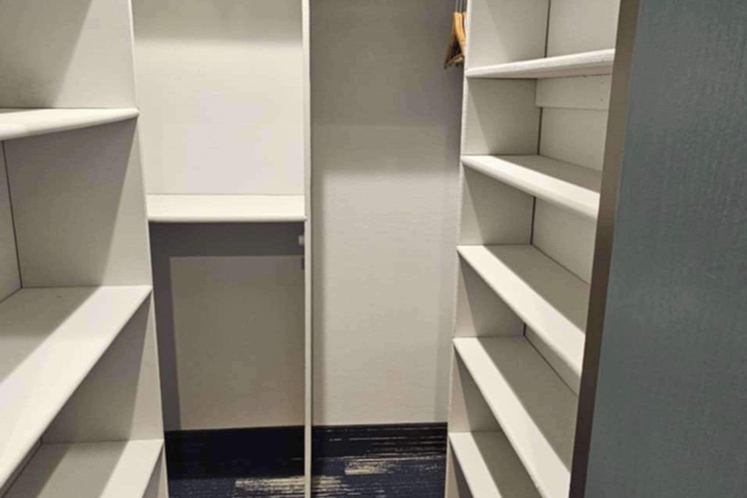 Un vestidor estrecho y vacío, con estanterías blancas y alfombra negra.