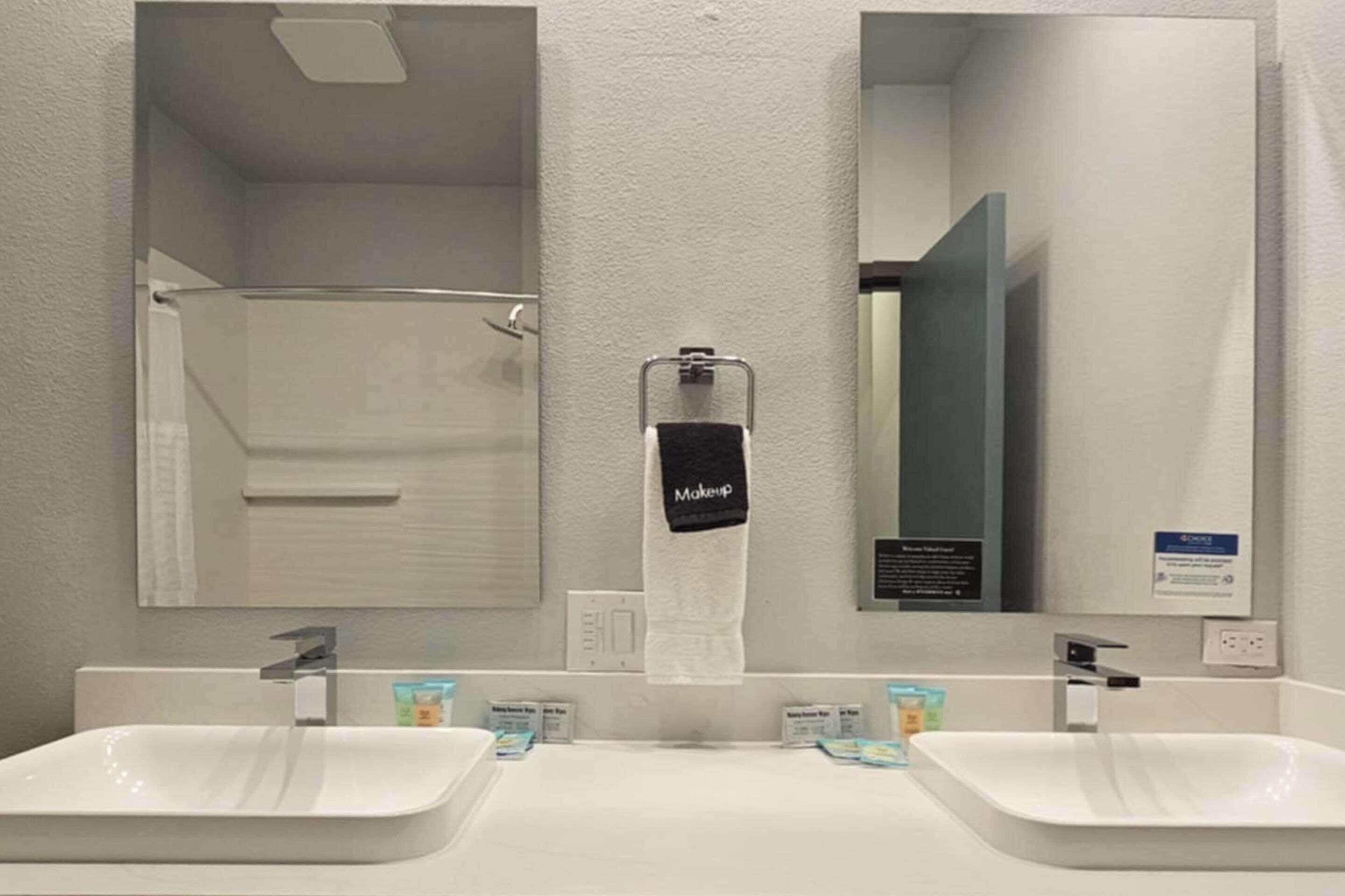 Un baño con dos lavamanos, un perchero con una toalla que dice 'Maquillaje' y un espejo.