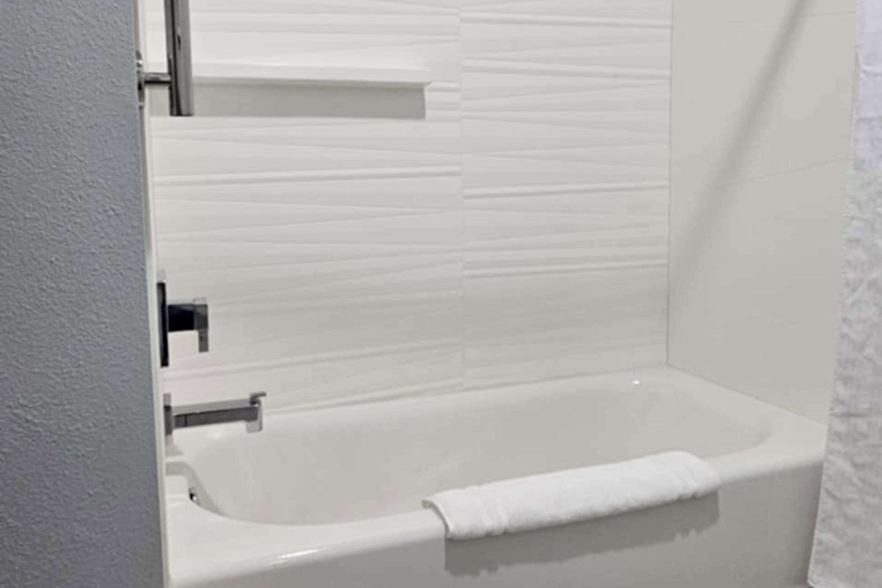 Een moderne badkamer met een badkuip, een douchegedeelte en een witte betegelde wand.