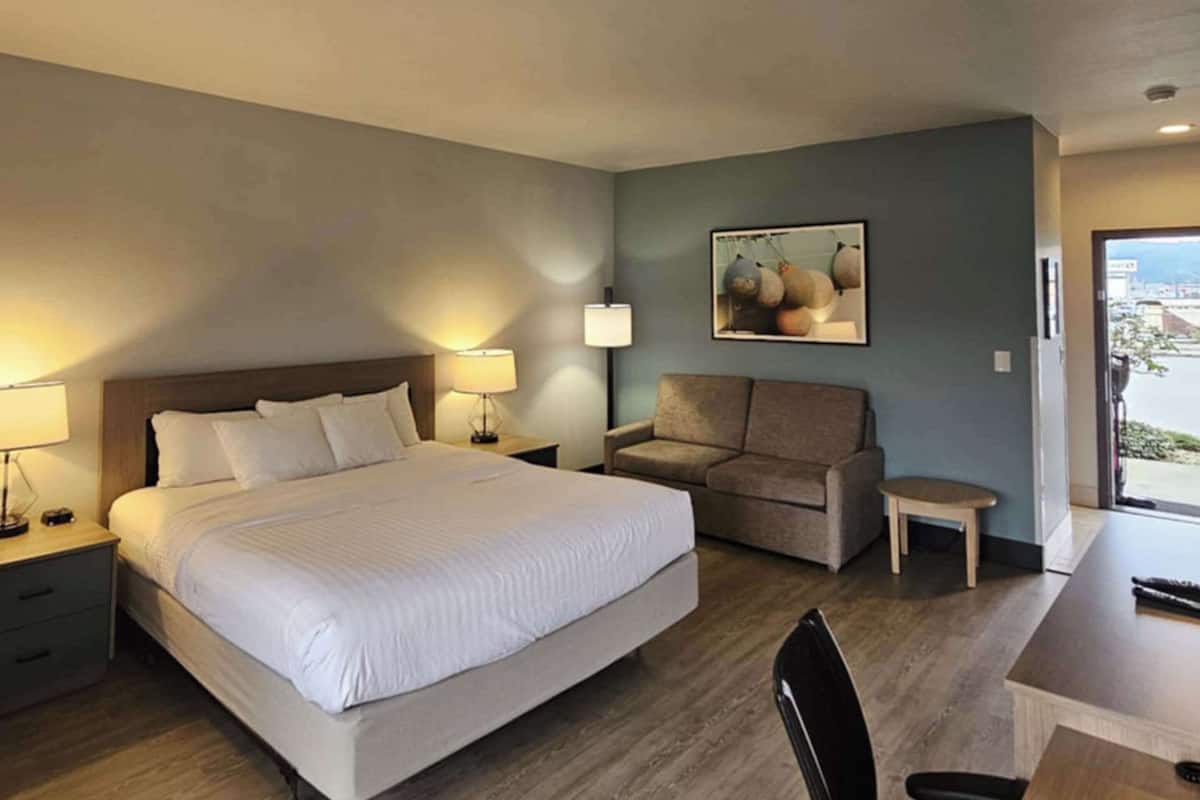 A hotel room with a large bed, a sofa, a desk, and a small table.