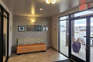 A lobby with a bench, framed pictures on the wall, and a view of the parking lot through the glass doors.