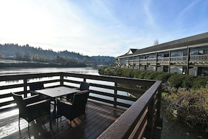 Una terraza de madera con una mesa y sillas que da a un río, con un edificio al fondo.