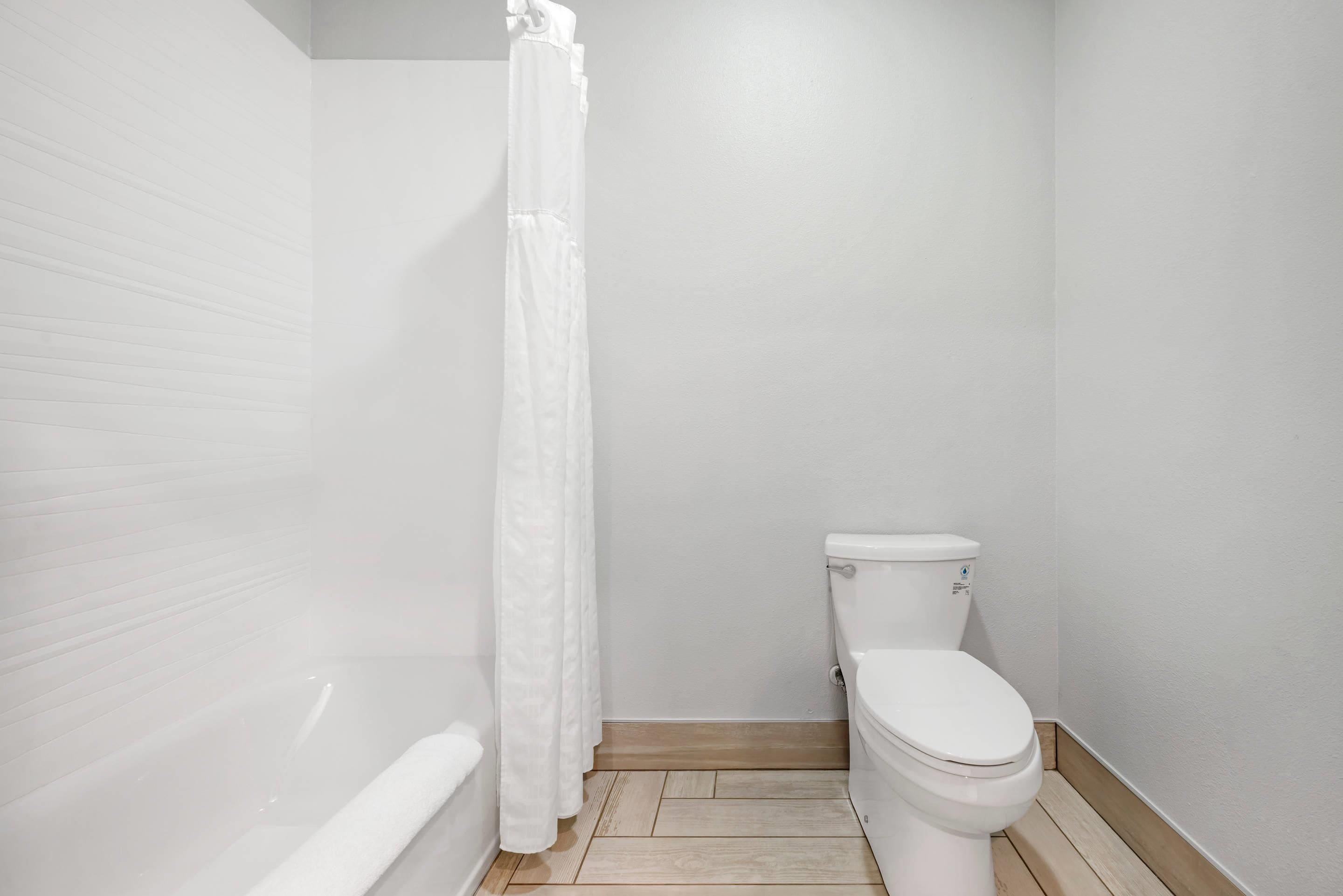 A small, clean bathroom with a white toilet, a bathtub, and a shower curtain.