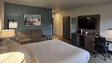 Habitación de hotel con una cama grande, un sofá, un escritorio con una silla, un televisor montado en la pared y un cuadro enmarcado.