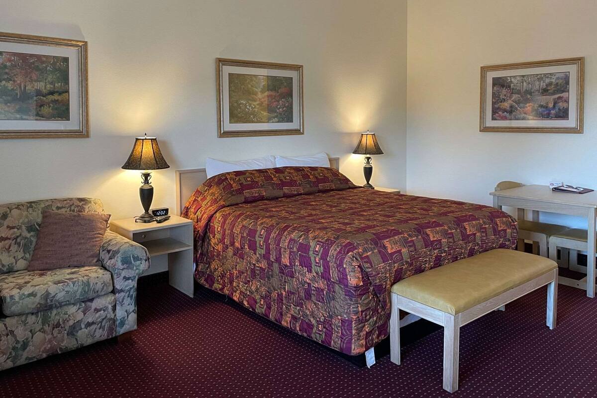 A hotel room with a bed, two nightstands, a chair, a desk, and a bench.
