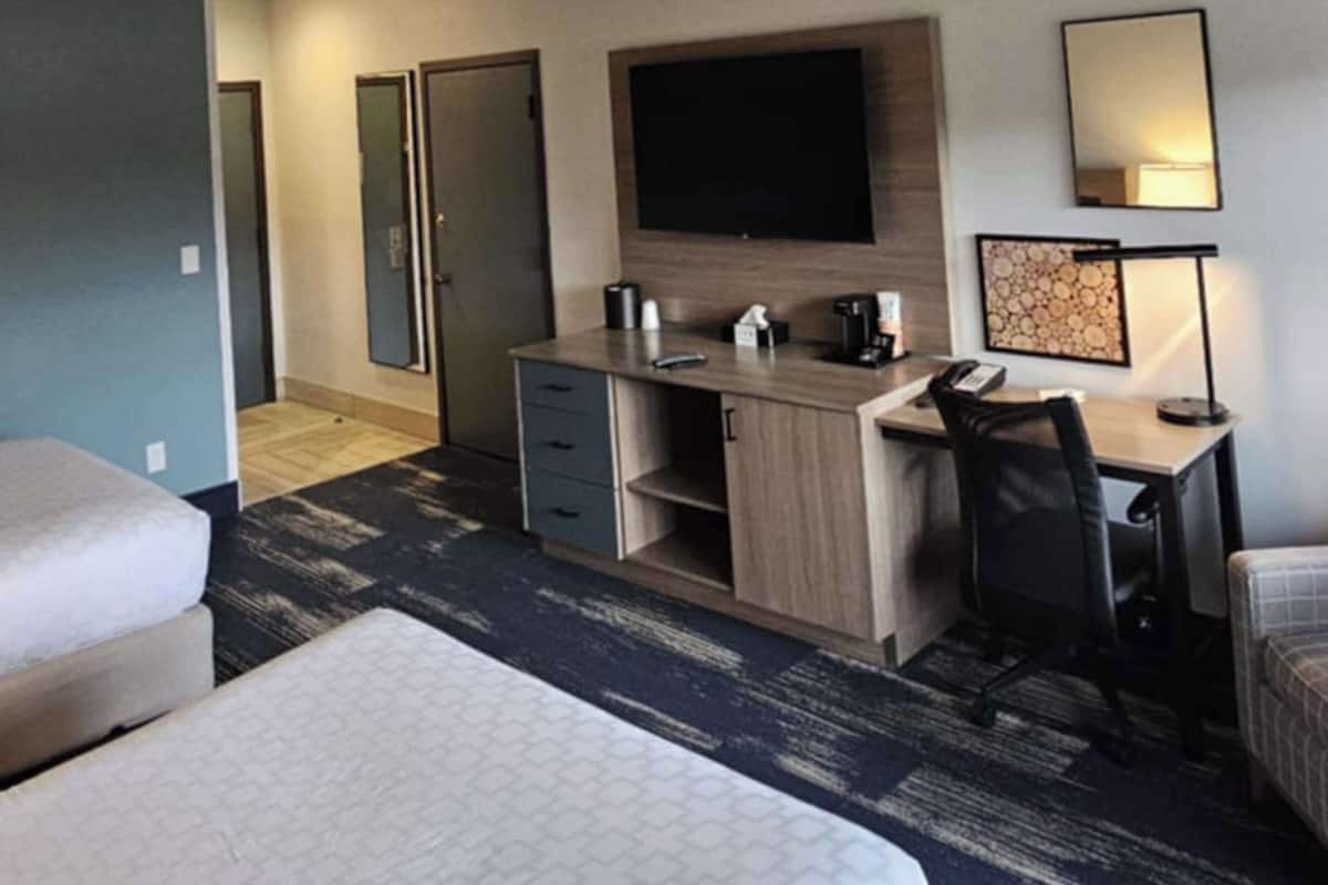 A hotel room with a bed, a desk with a chair, a flat-screen TV, a coffee maker, and a lamp.