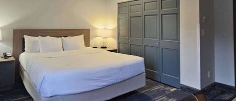 A hotel room with a large bed, a wardrobe, a nightstand with a lamp, and a chair.