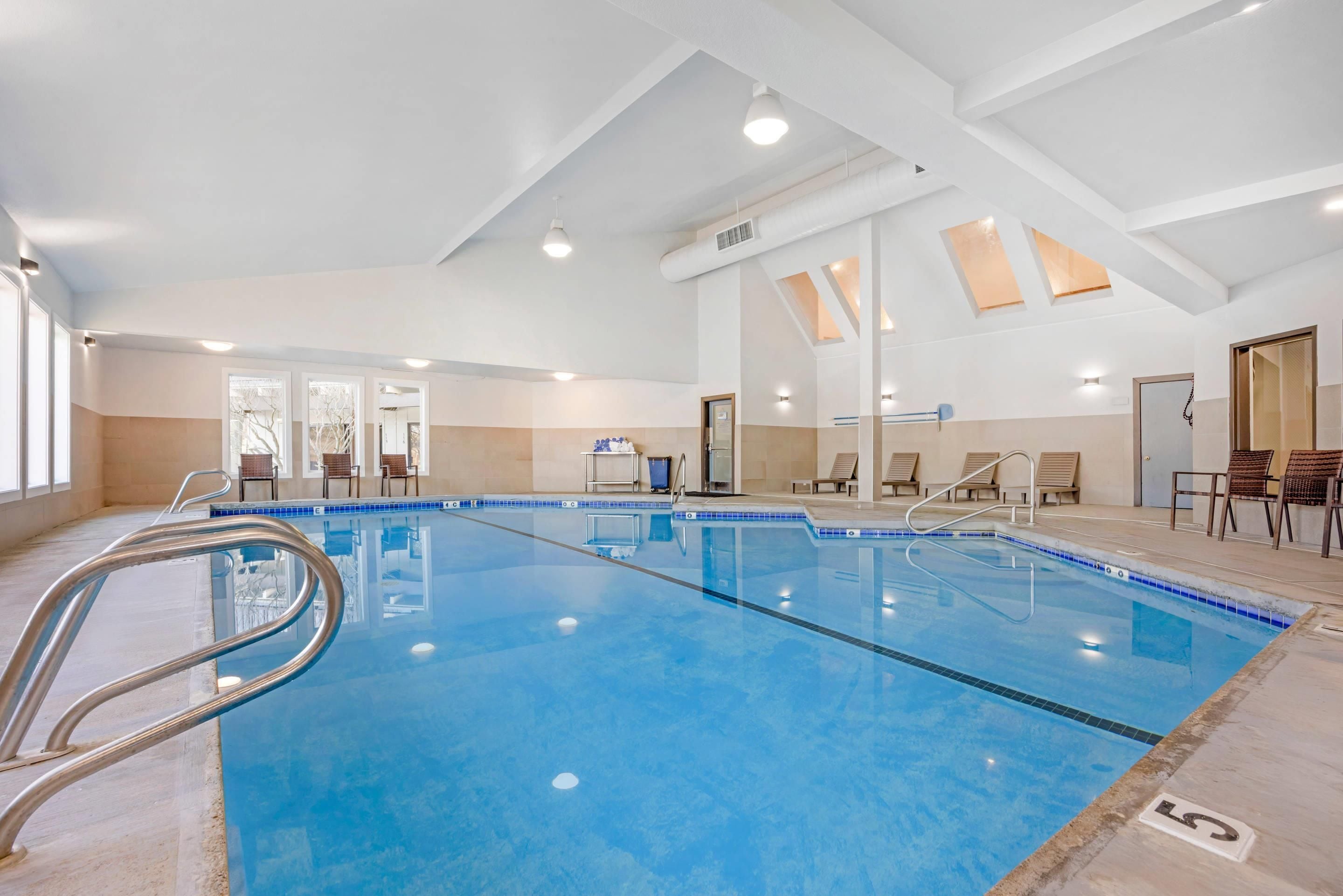An indoor swimming pool with clear water, a metal ladder, and lounge chairs around the perimeter.