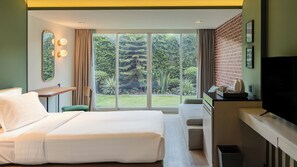 A hotel room with a bed, a desk, a TV, and a large window with a view of greenery.