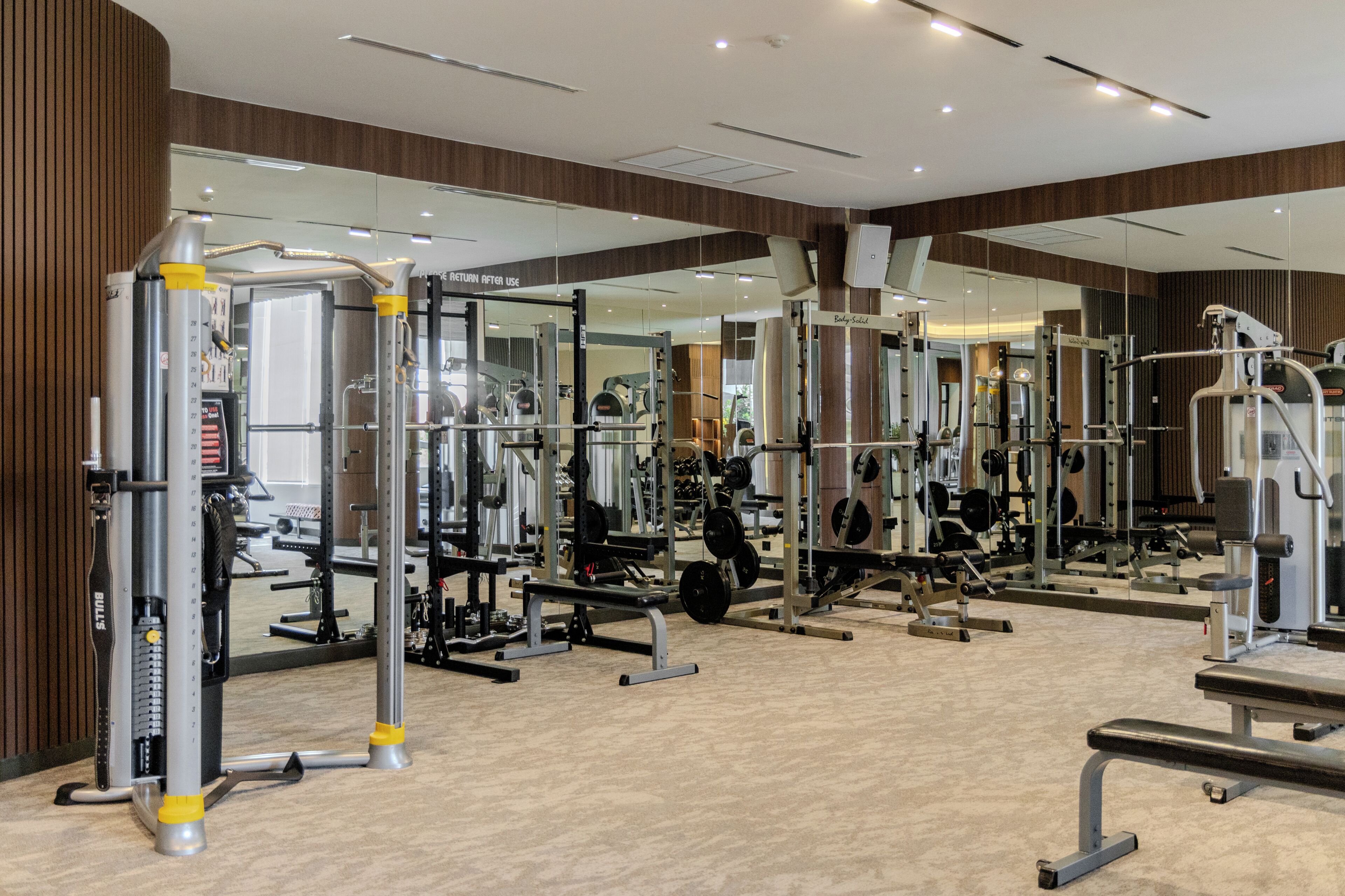 Un gimnasio con diversos equipos de ejercicio, espejos y una pared de madera.