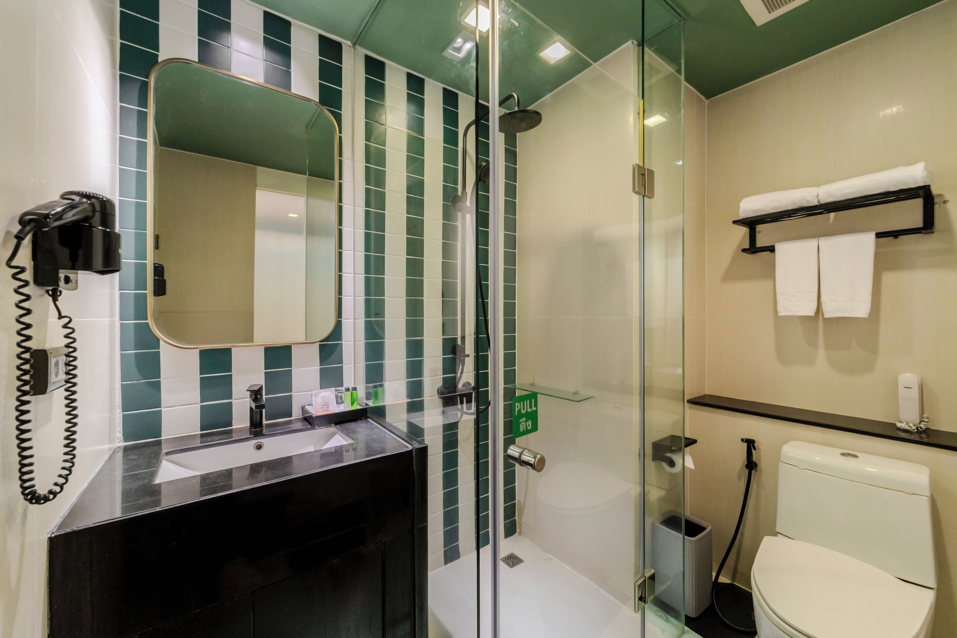 A bathroom with a glass-enclosed shower, a sink with a mirror, a towel rack, and a toilet.