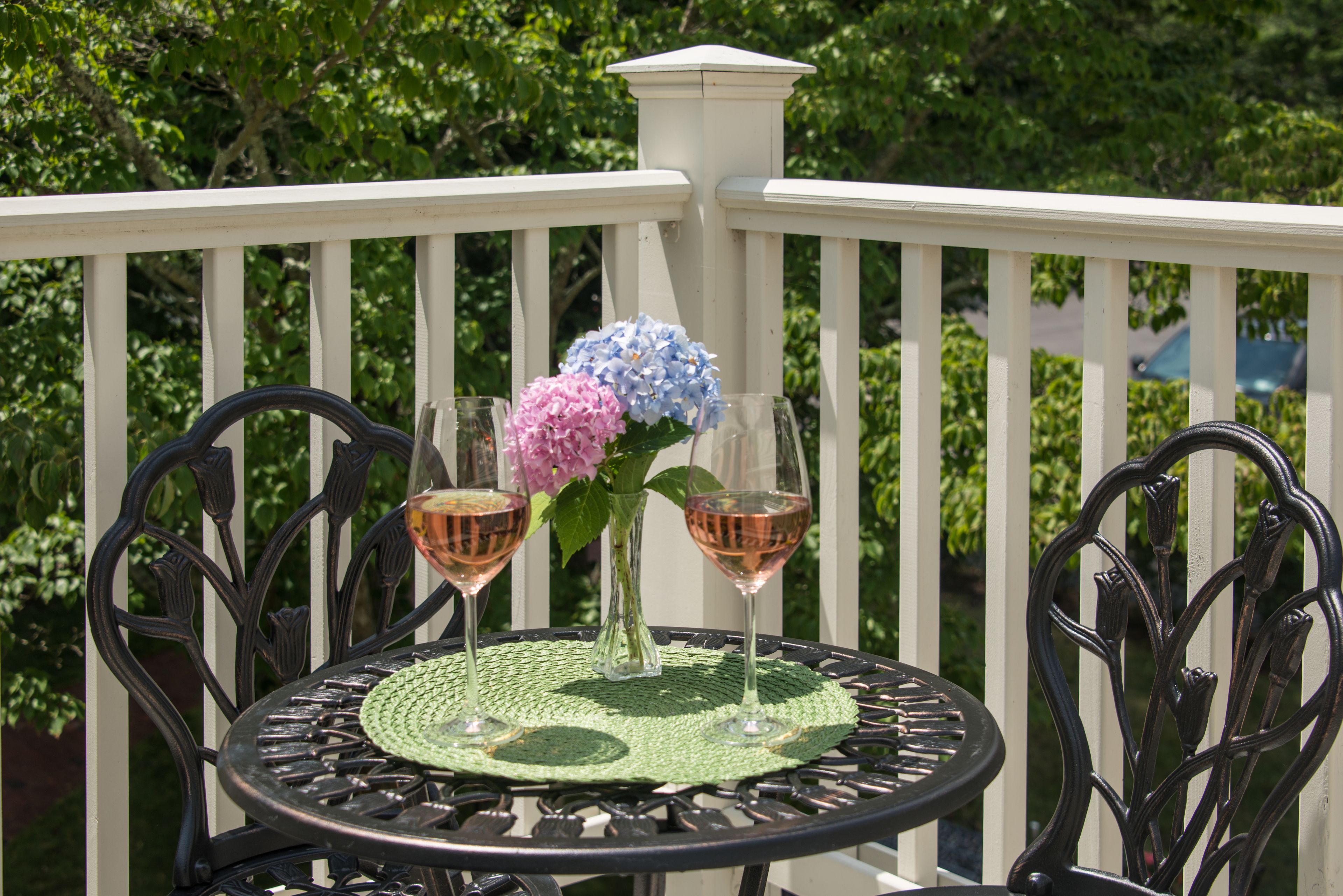 A round table with a green mat, two glasses of wine, and a vase with flowers on a balcony.