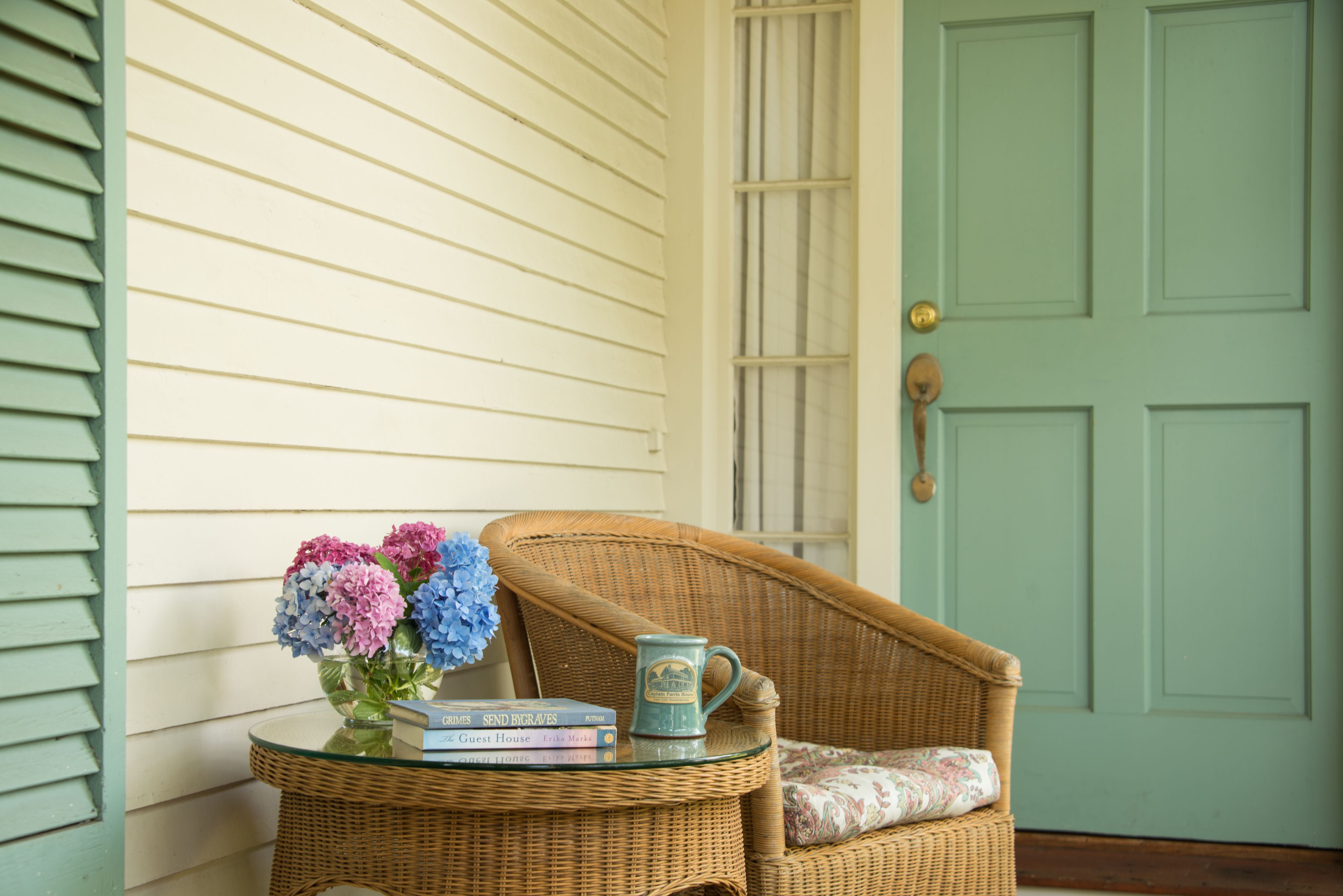 A wicker chair with a cushion, a glass table with a vase of flowers, and a few books.