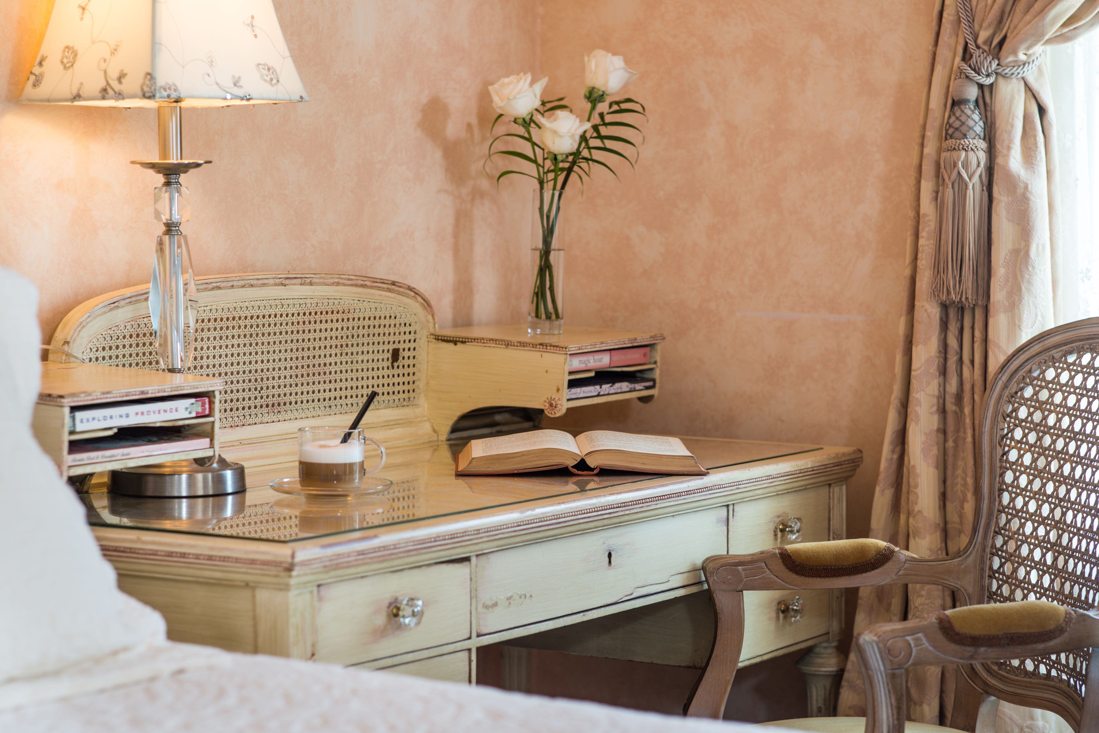 Una habitación de estilo vintage con un escritorio de madera, una lámpara, un jarrón con flores y una silla.