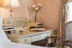 Una habitación de estilo vintage con un escritorio de madera, una lámpara, un jarrón con flores y una silla.