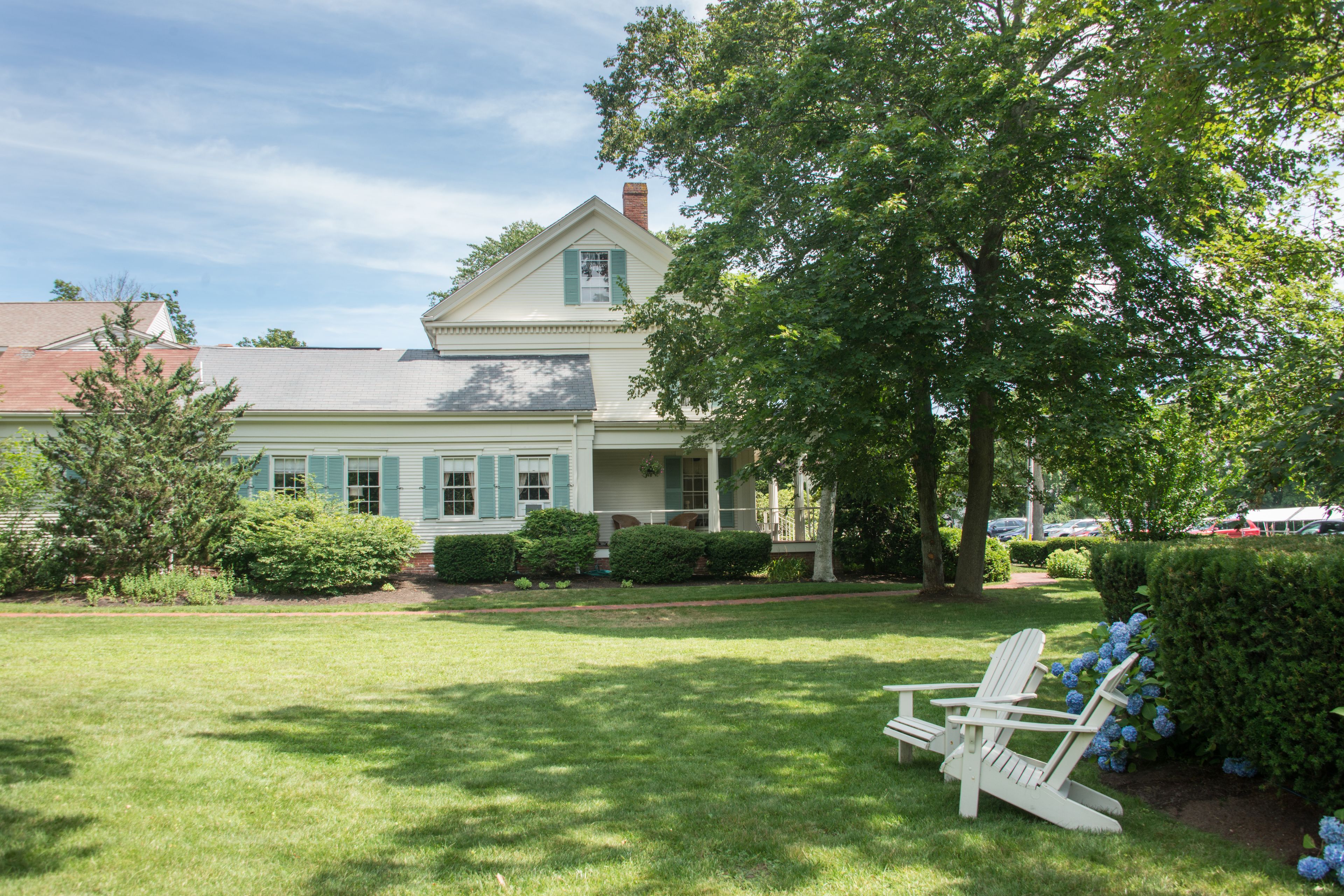 Ein zweistöckiges Haus mit Veranda, Rasen und einem weißen Adirondack-Stuhl.