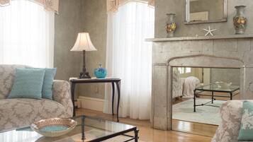 A living room with patterned sofas, a glass coffee table, a lamp, and a fireplace with a mirror above.