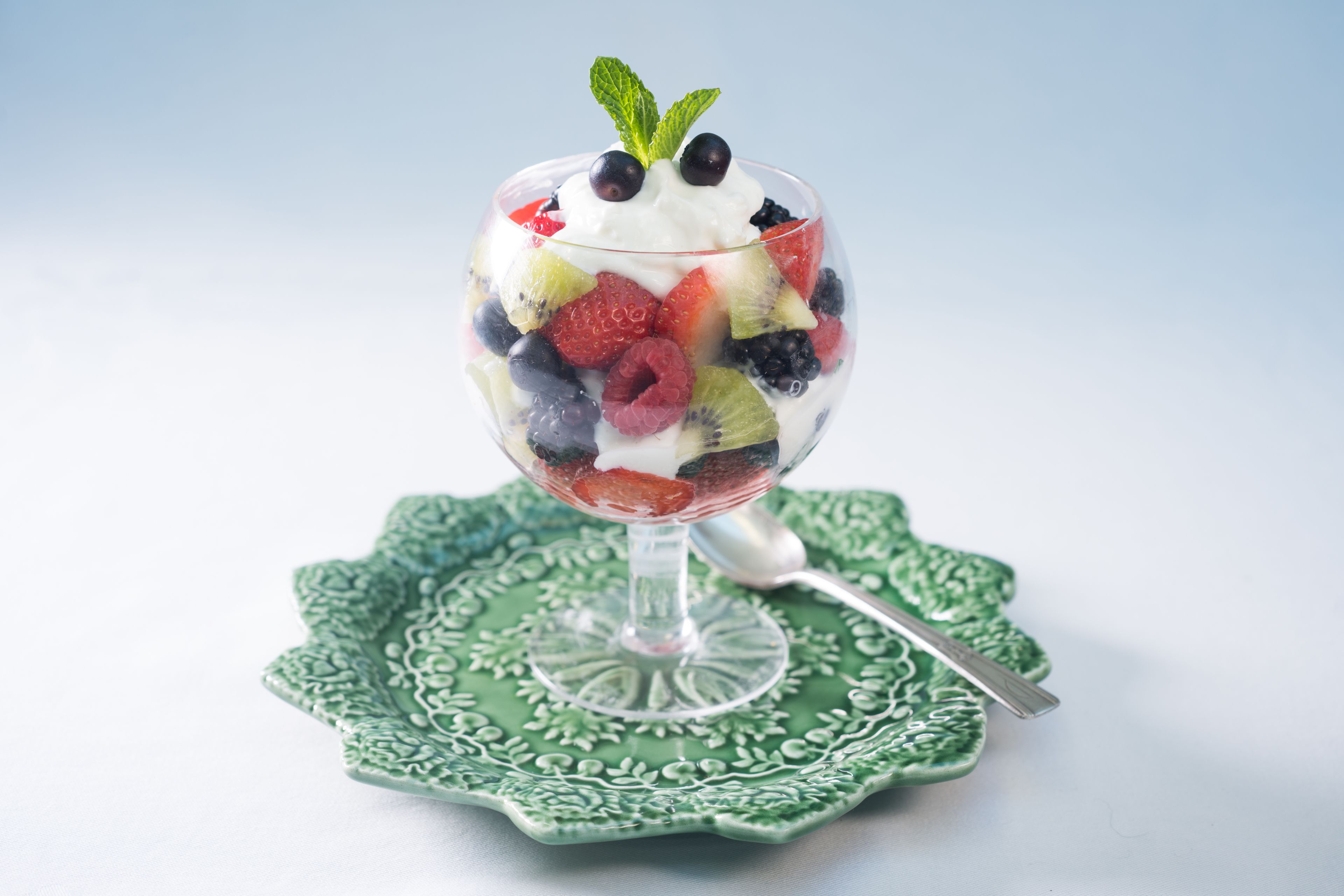 A dessert in a glass bowl on a green plate with a spoon.