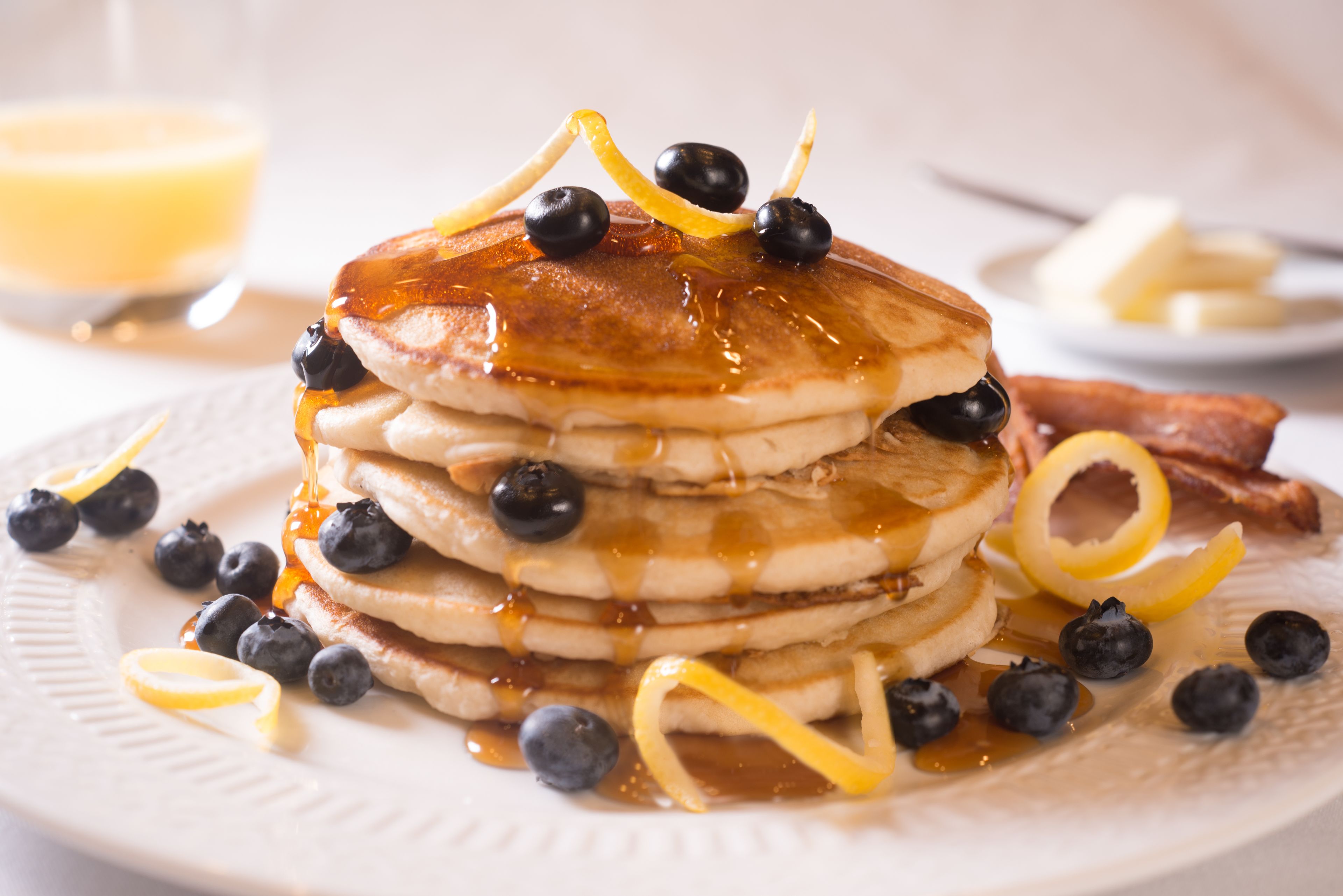 A stack of pancakes with blueberries and lemon zest on a plate.