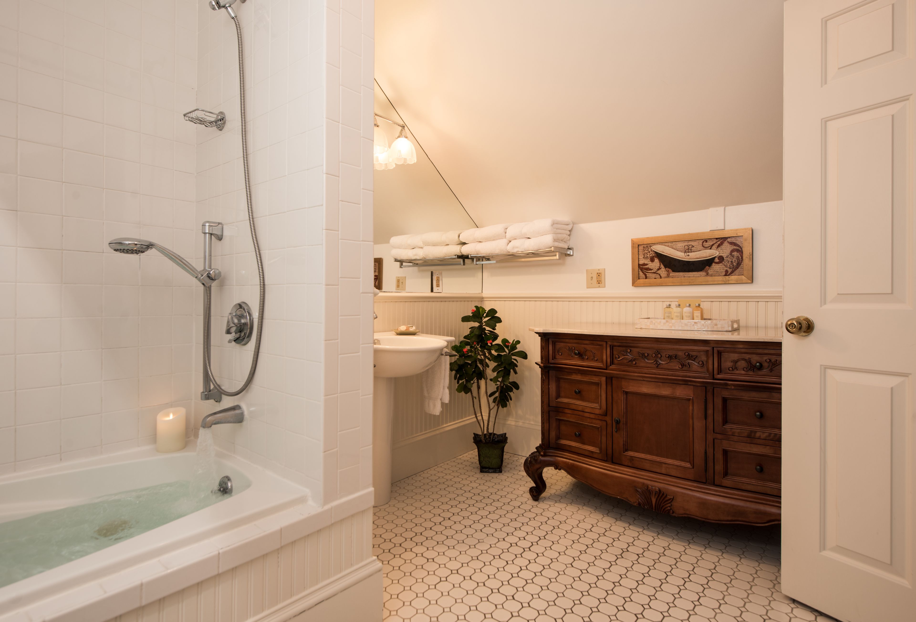 A bathroom with a bathtub, a sink, a vanity with drawers, a potted plant, and a towel rack.