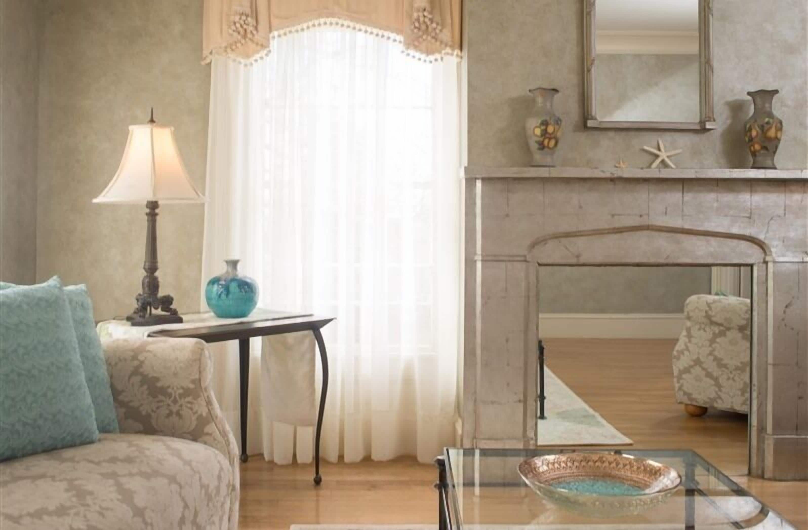 A living room with a sofa, a table with a lamp, a glass coffee table, and a fireplace with decorative items.