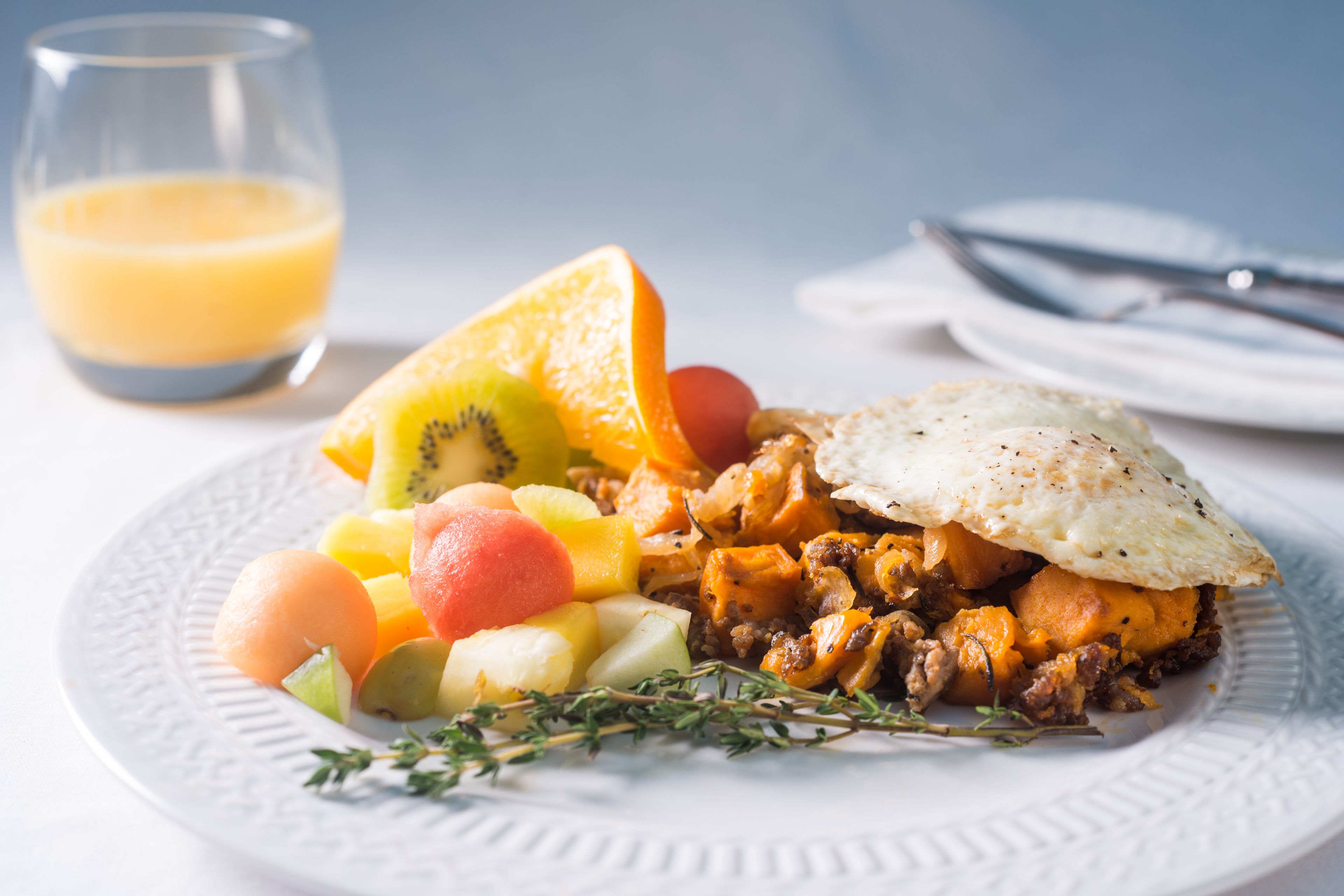 A breakfast plate with various fruits, a fried egg, and a glass of orange juice.