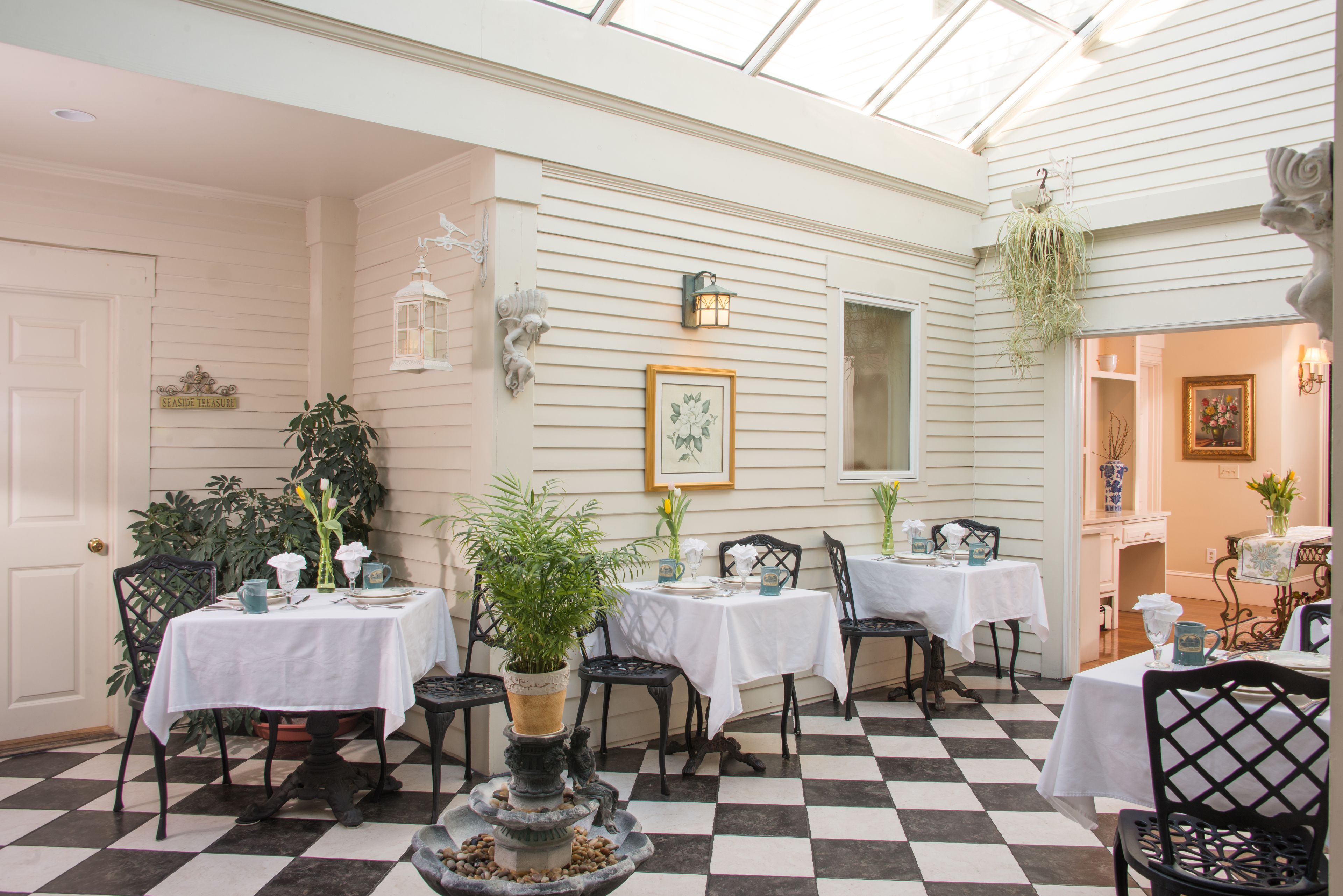 A dining area with tables and chairs, a checkered floor, and a white wall with a framed picture.