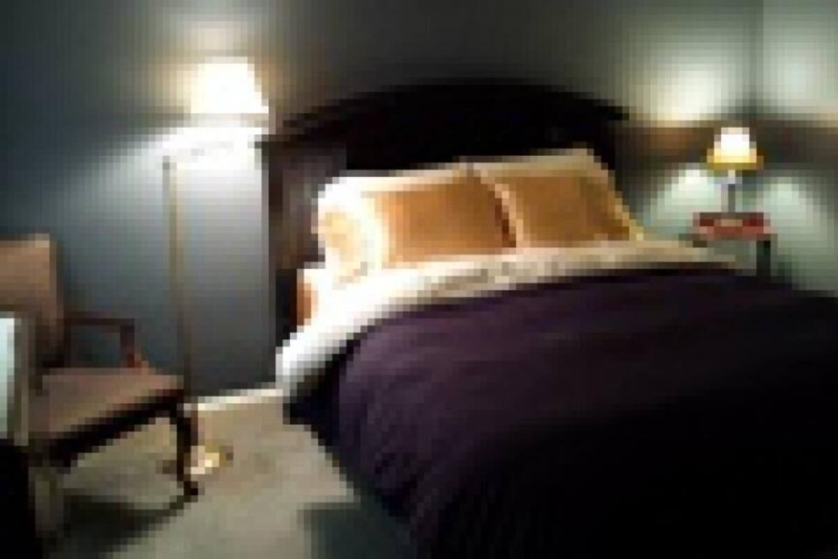 A neatly made bed with a dark headboard, a bedside table with a lamp, and a chair in a room with blue walls.